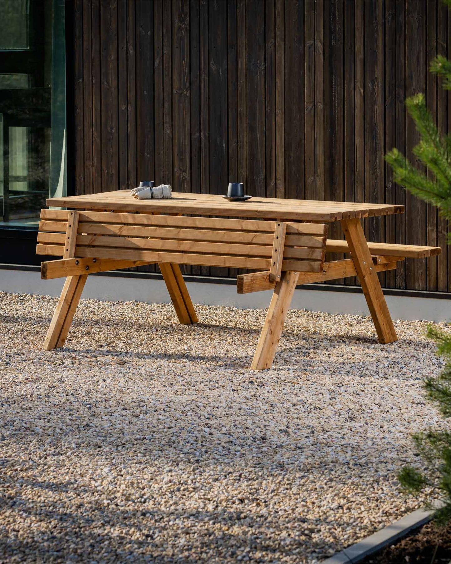 Brown picnic table sitting on small pebbles next to a wooden house