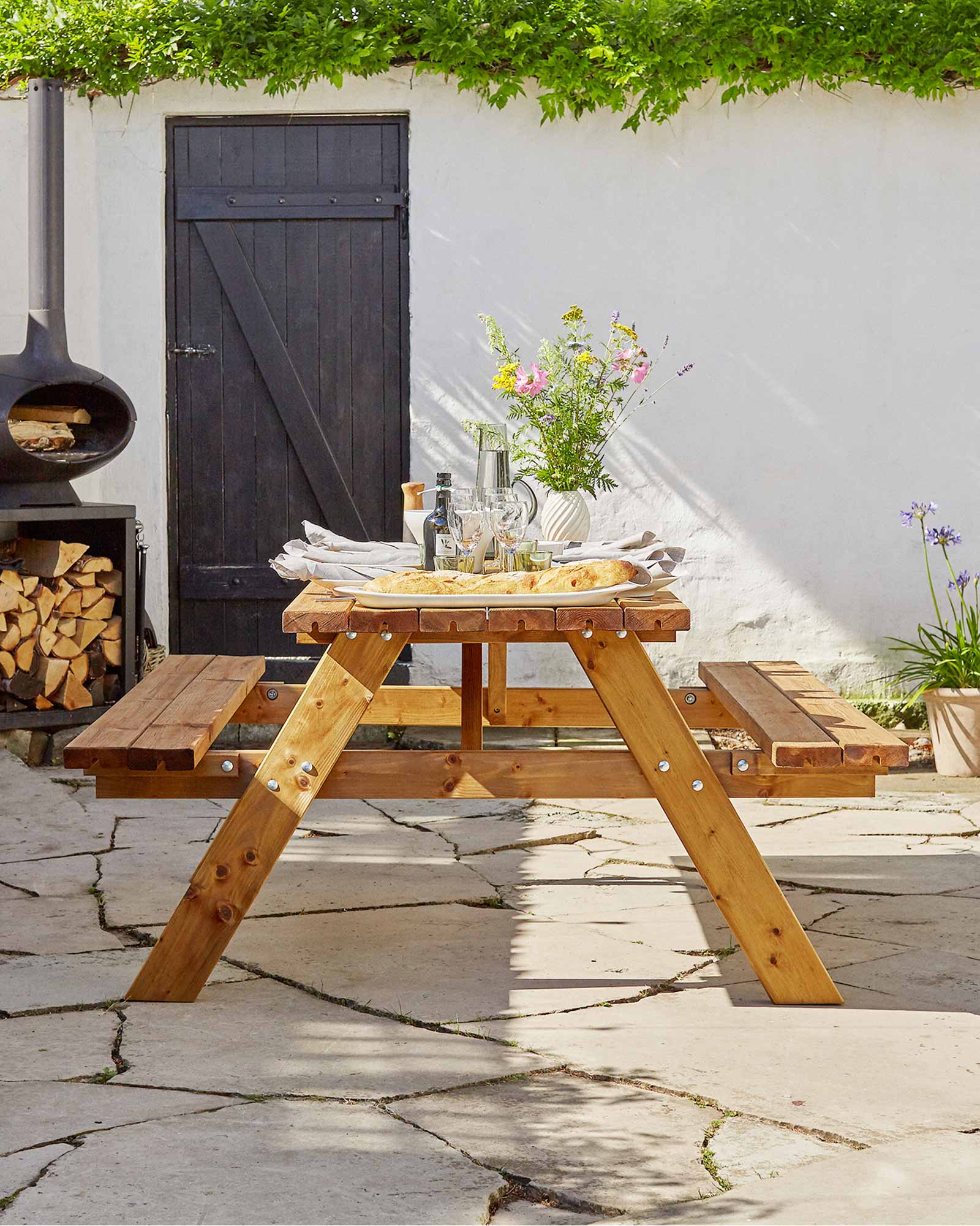A brown picnic table with flowers and food served.