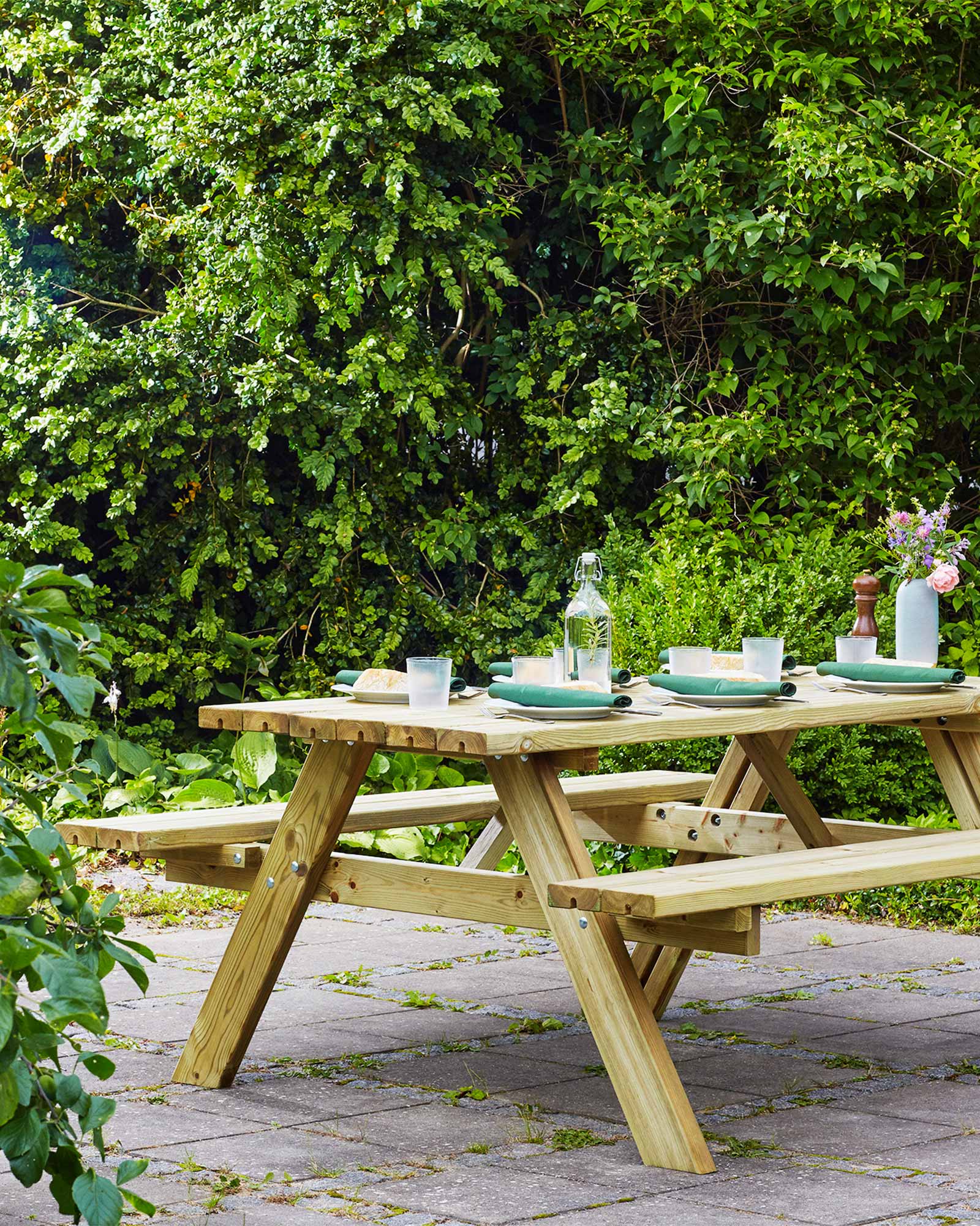Green wood picnic table setting surrounded by green bushes