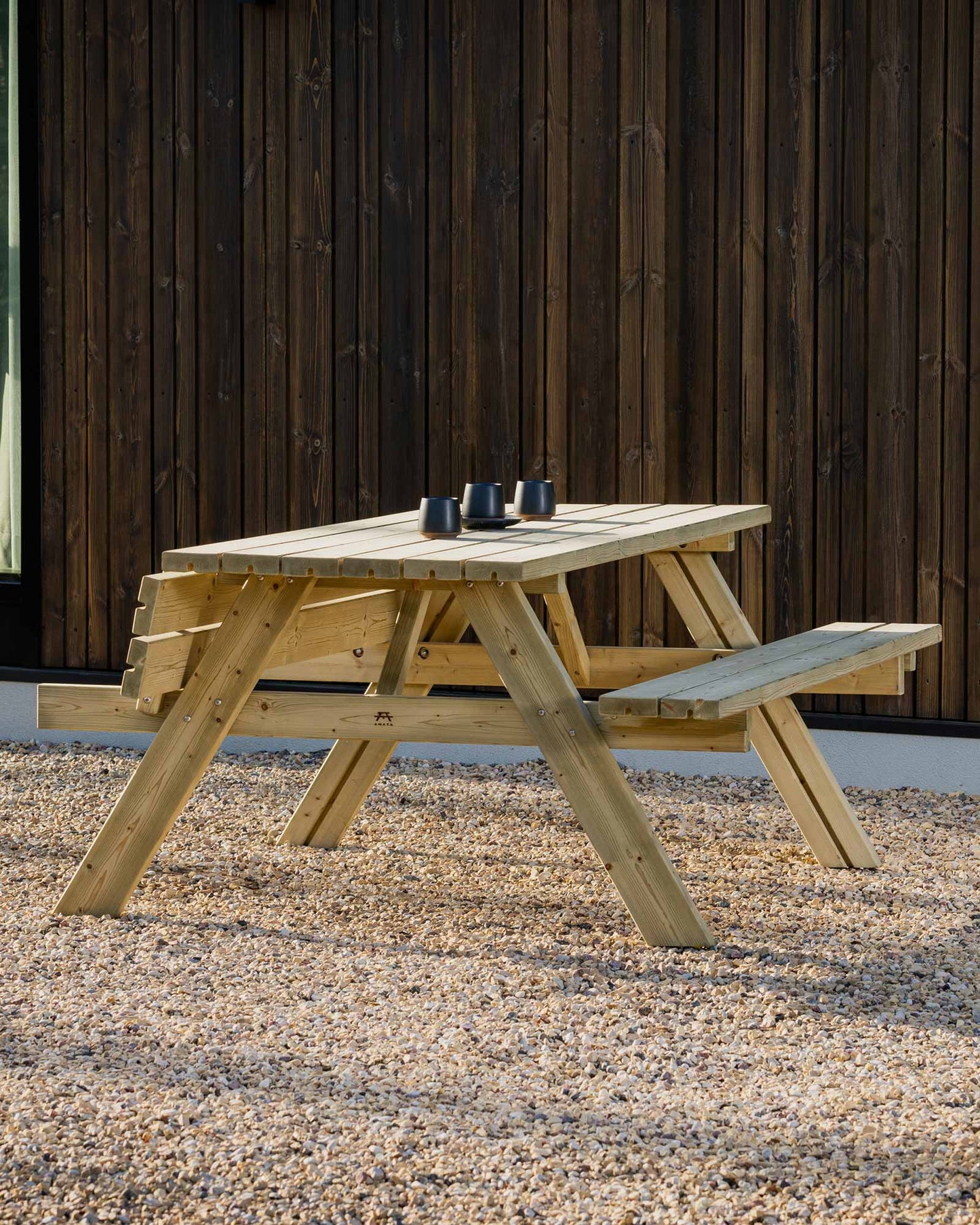 Green picnic table with 3 black espresso mugs on pebble ground