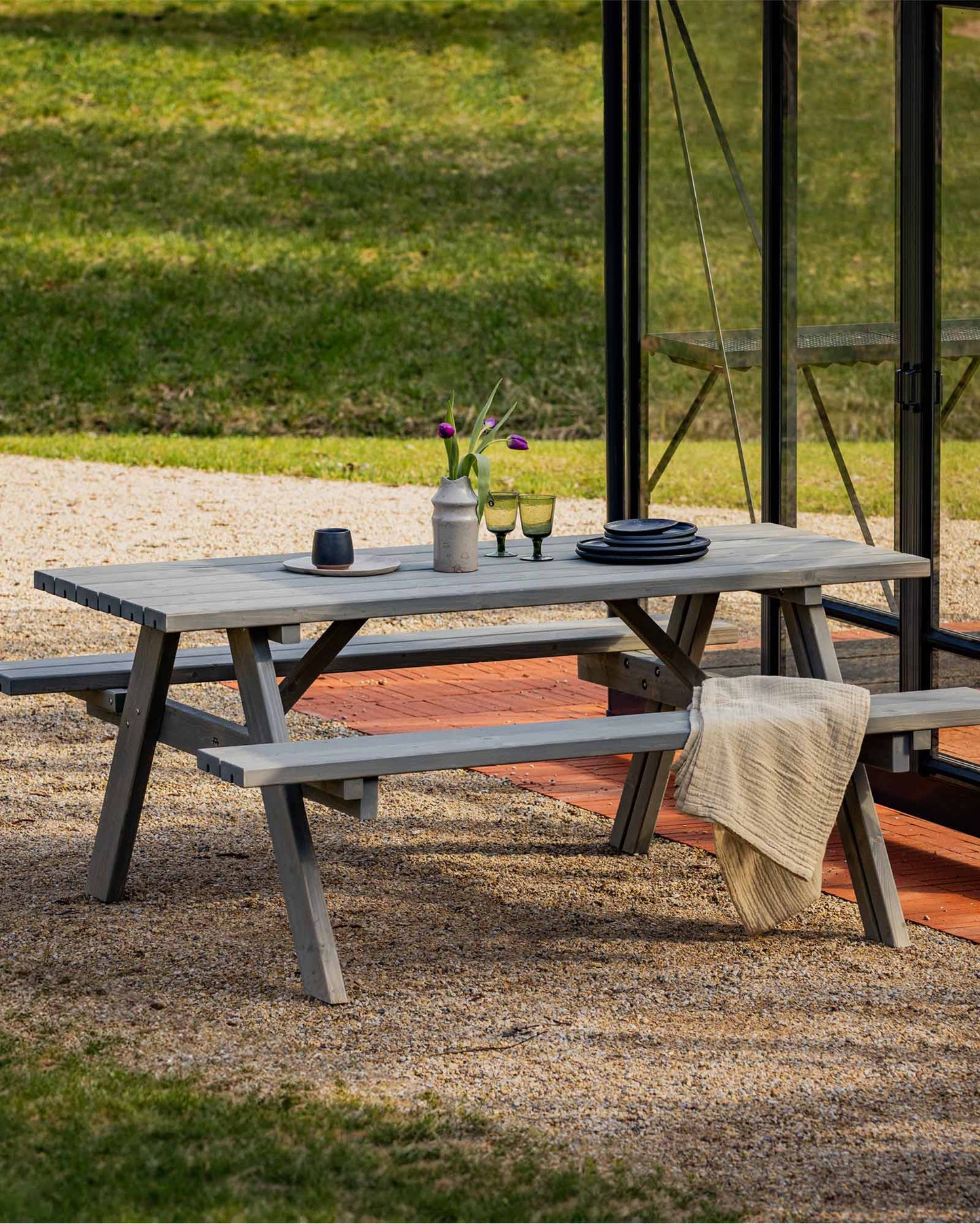 Grey picnic table and bench set next to a glass greenhouse