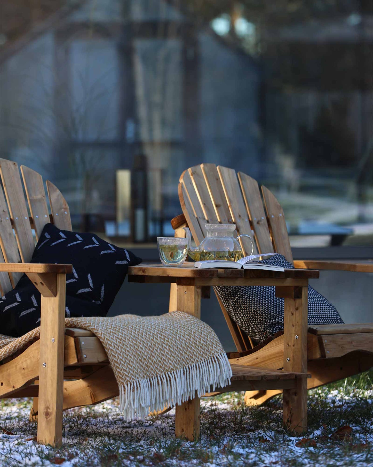Double wooden Adirondack chair set in brown, decorated with throw pillows and blankets outside in winter