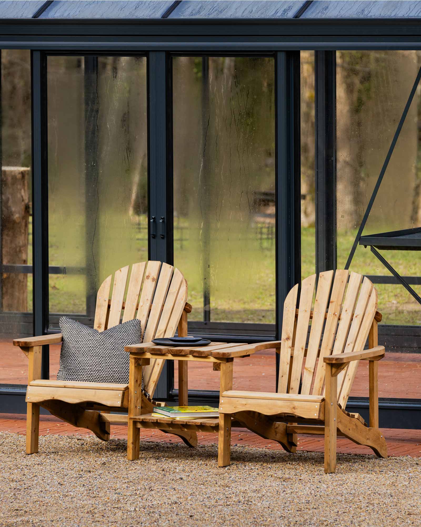 Double brown Adirondack chair set next to a modern glass greenhouse