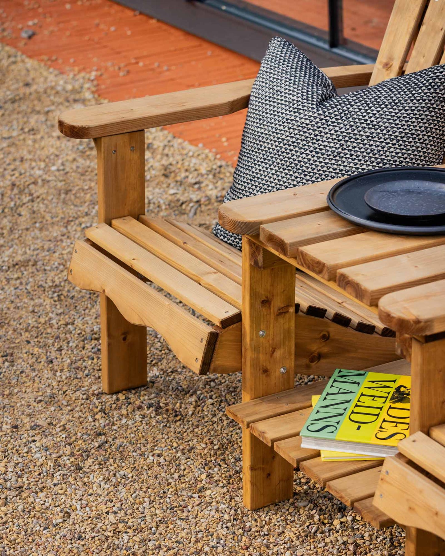 Closeup of the brown double Adirondack chair with a book and black plates