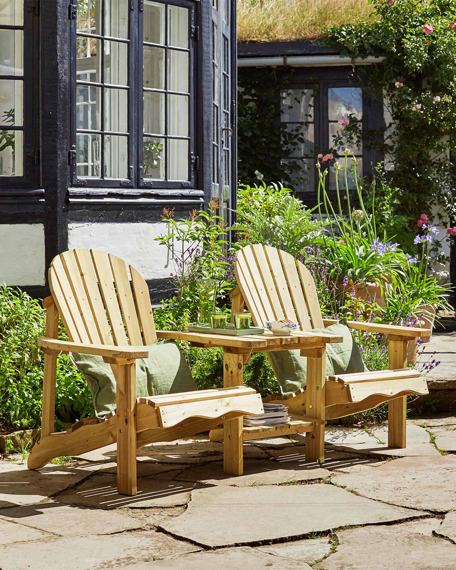 Double green Adirondack chair next to a house and flower bed