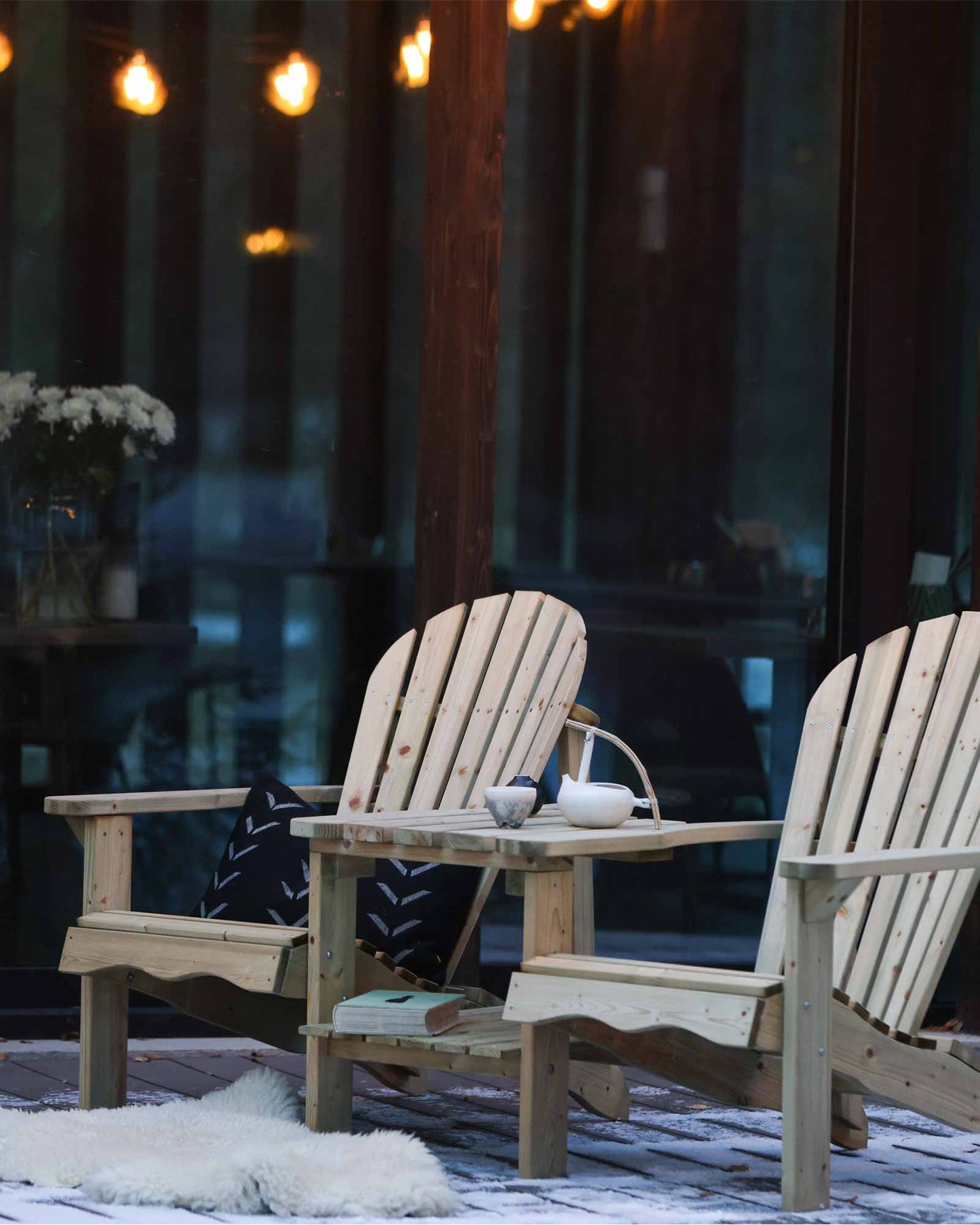 Green double wooden Adirondack chair set with a teapot and cup outside in winter at a slight angle