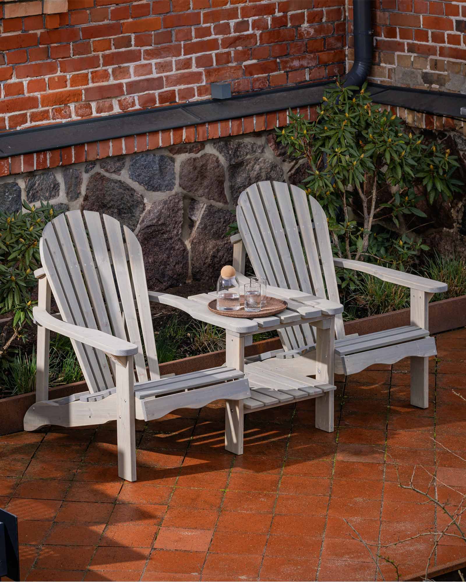 Double grey Adirondack garden chair set sitting on a bright red brick tile patio