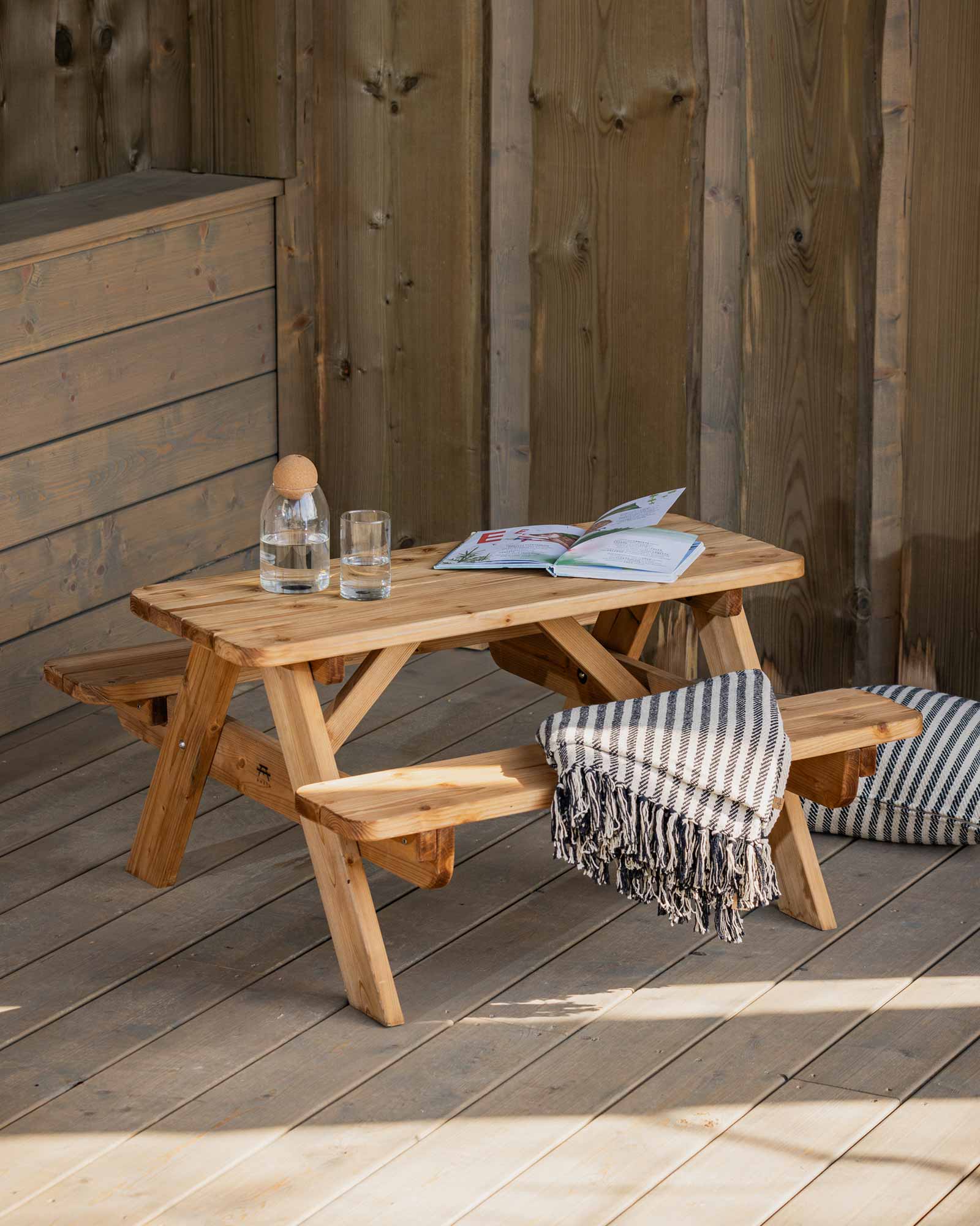 Mini brown wood picnic table on a patio with a water glass and a throw