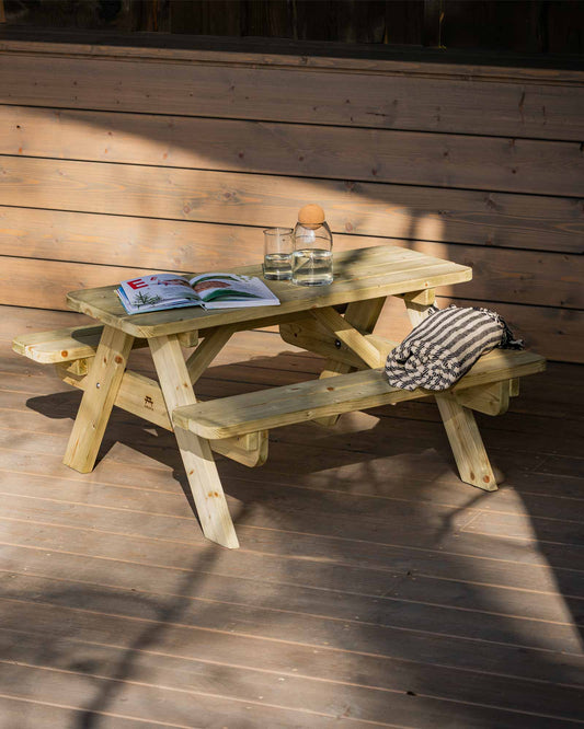 Mini green picnic table on a patio with an open picture book, a throw blanket and water jug on top