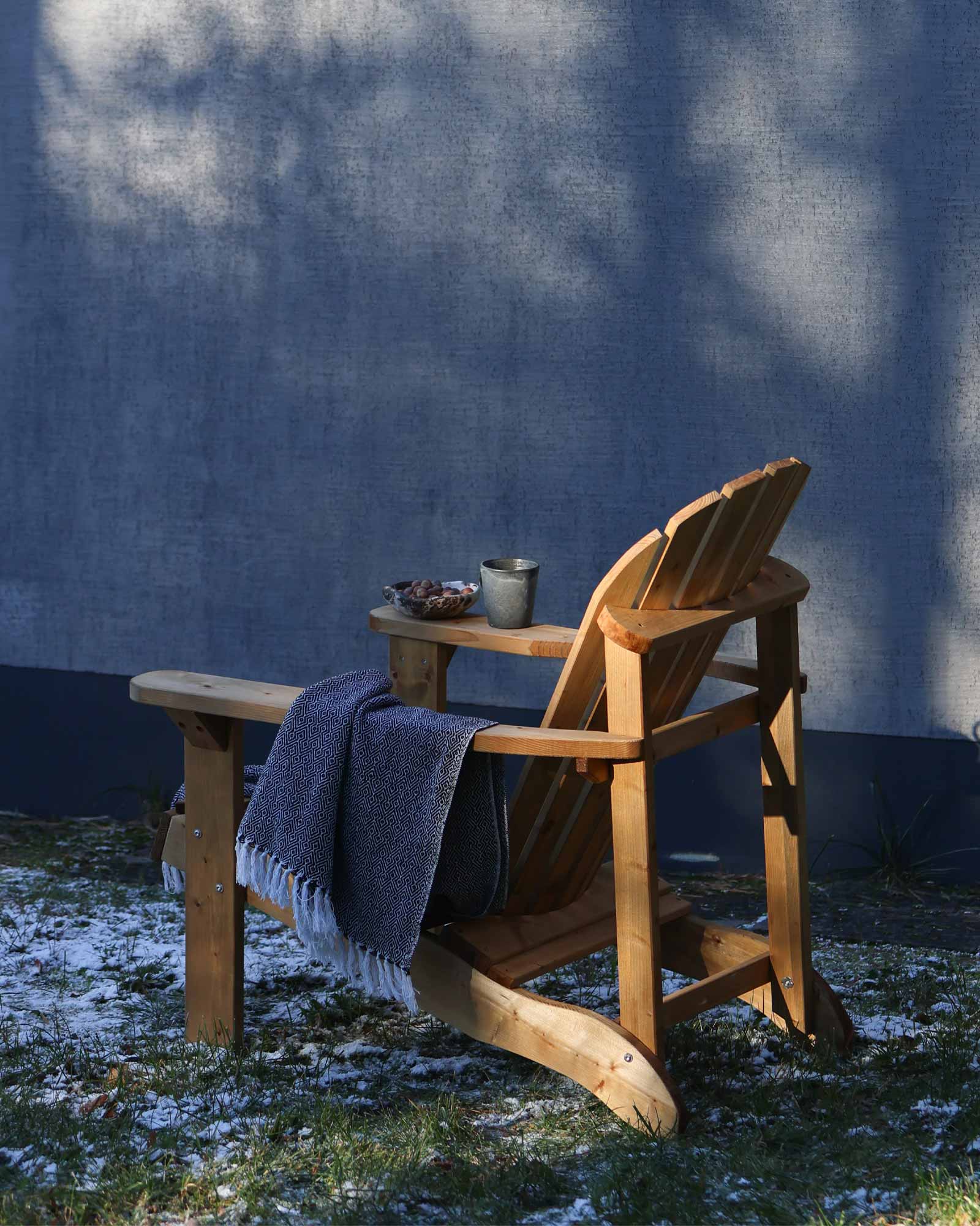 Brown wooden Adirondack chair with a cup of tea and throw blanket on a snowy grass