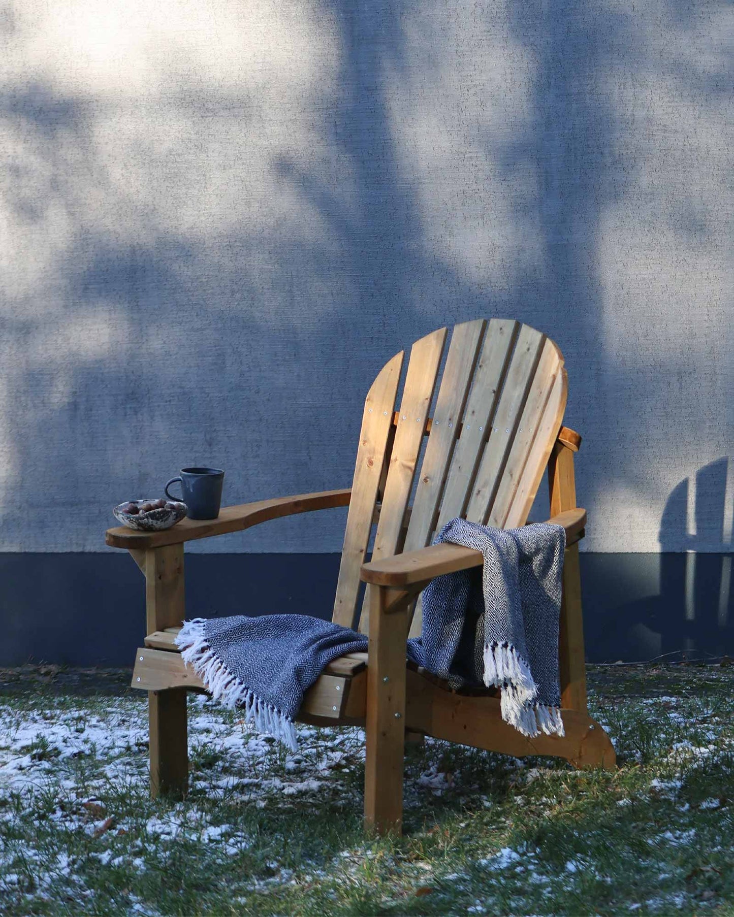 Brown wooden Adirondack chair with a throw blanket and cup of tea next to a grey house