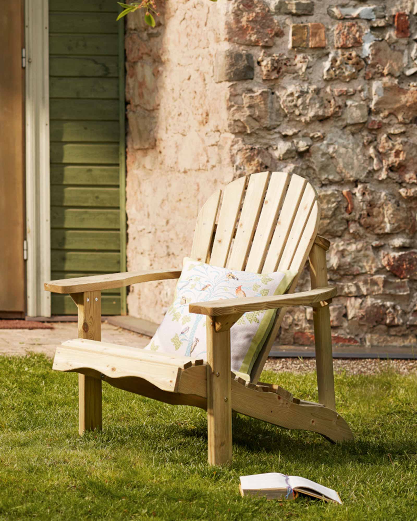 Green Adirondack chair with a decorative throw pillow, sitting on the grass