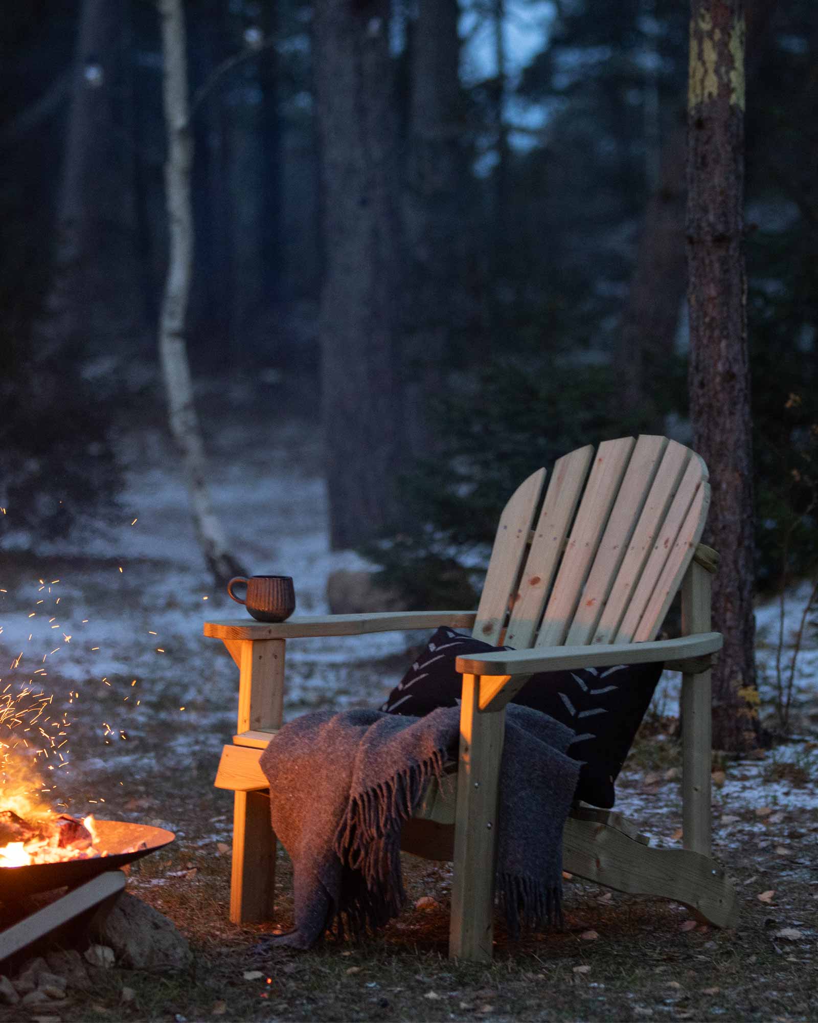 Green Adirondack garden chair next to a fireplace with a throw pillow and blanket