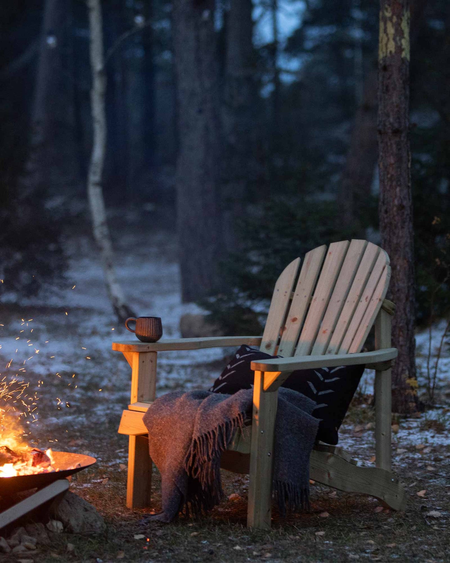 Green Adirondack garden chair next to a fireplace with a throw pillow and blanket