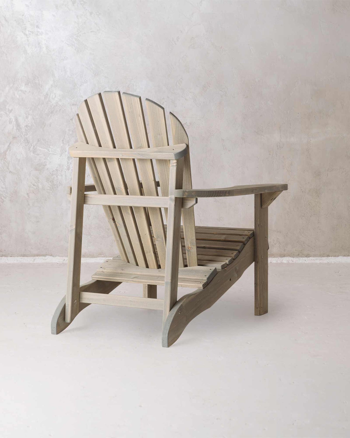 Grey wooden Adirondack chair on a concrete background, photographed from the back and at a slight angle