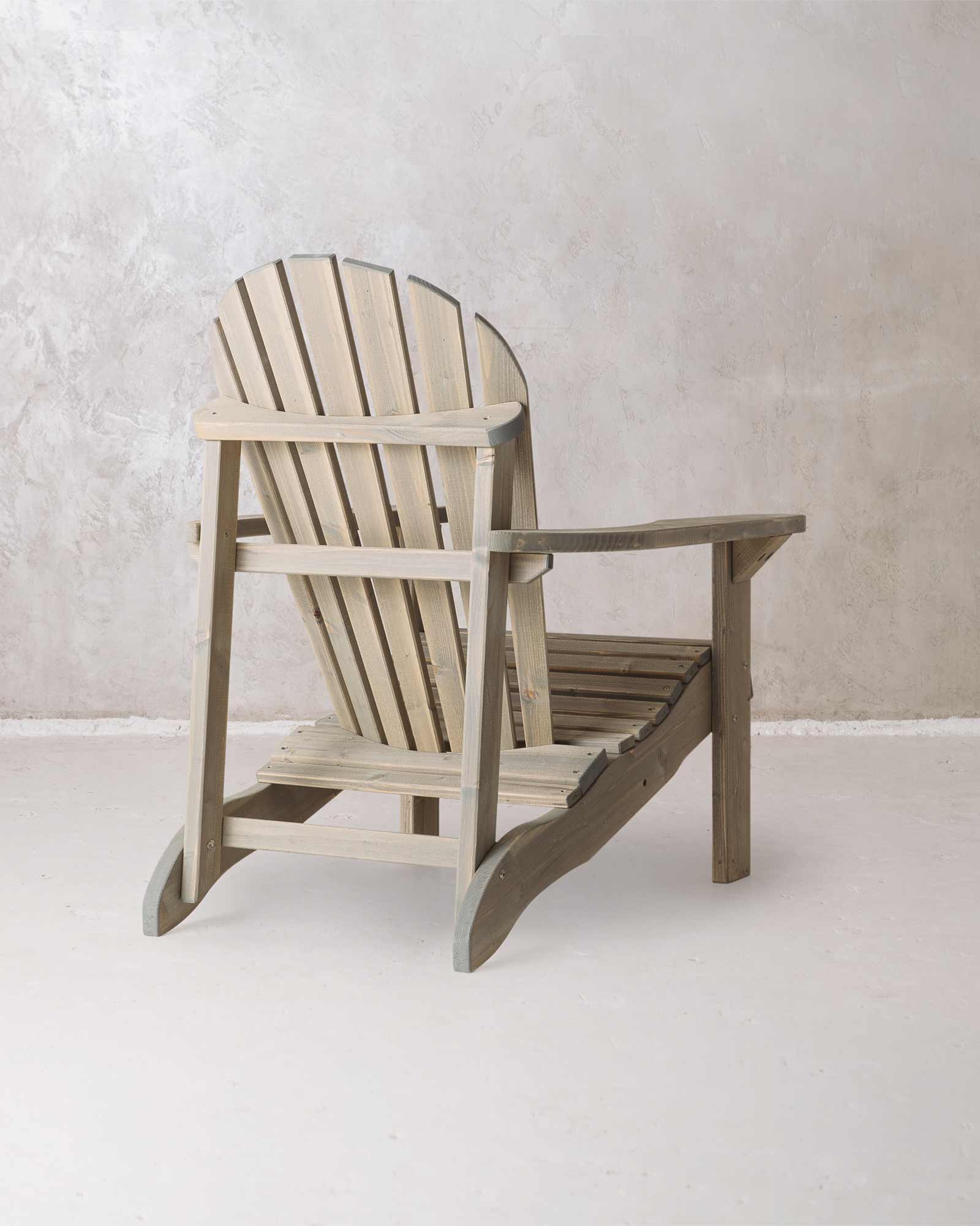 Grey wooden Adirondack chair on a concrete background, photographed from the back and at a slight angle